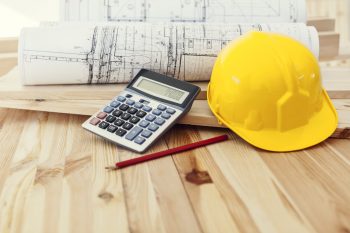 Yellow helmet with blueprints and calculator on wood